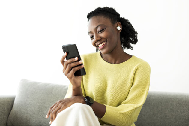微笑戴着无线耳塞用手机的女人放松非洲裔美国人黑色