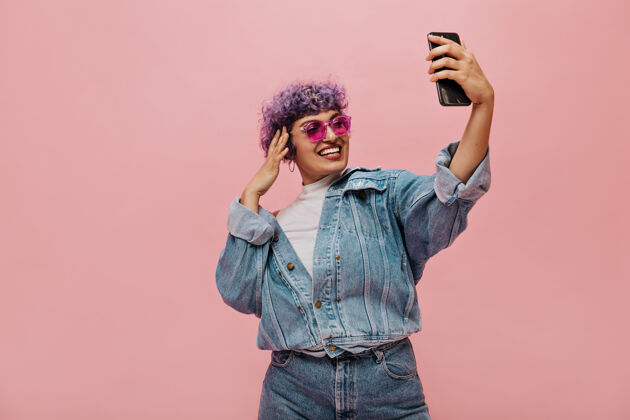 短发一个戴着太阳镜的紫色头发的现代女人在粉色上拍照一个穿着宽大明亮衣服的微笑女人在自拍活跃年轻人歌曲
