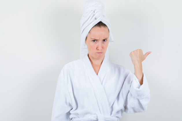前面身穿白色浴袍的年轻女子 毛巾用拇指指向一边 神情可疑 正前方视图欢呼拇指优雅
