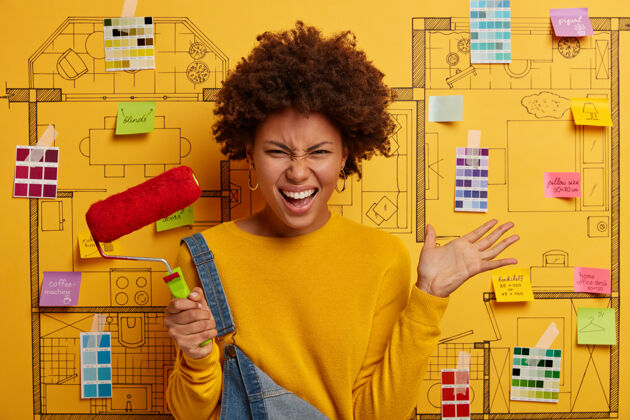 翻新恼怒的女人卷曲的非洲发型 举着手掌 握着油漆辊 翻修墙壁 穿着随意 反对房屋设计项目画笔素描绘画