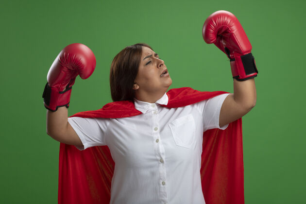 女自信的中年女超级英雄戴着拳击手套站在格斗姿势孤立的绿色背景拳击姿势自信