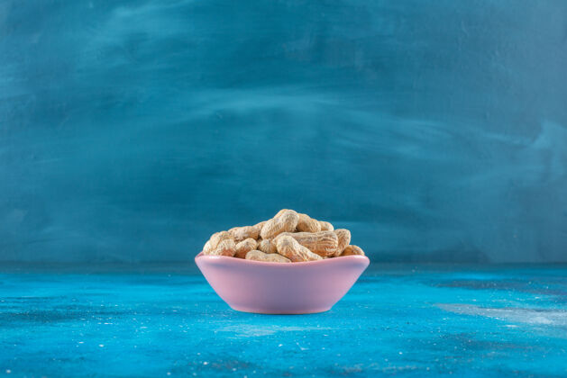 坚果花生壳在盘子里放在蓝色的表面上自然贝壳花生