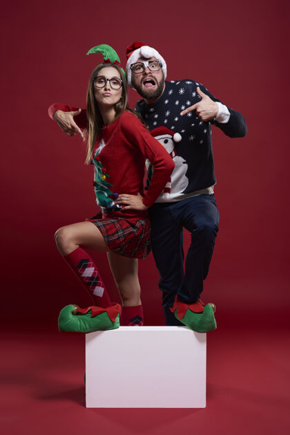 情侣一对穿着奇怪圣诞服装的年轻夫妇踩着一个空立方体书呆子圣诞节女人