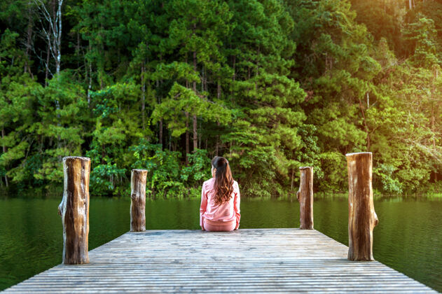 时髦一个女孩独自坐在湖边的木桥上泰国 庞昂独自平静湖泊