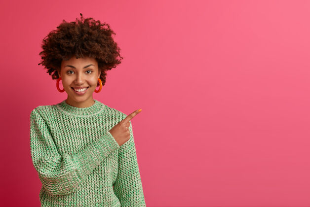 高兴幸运快乐的黑皮肤女人点着幸福的表情 为你的广告展示复制空间 推荐访问购物网站 点击链接 在玫瑰色的墙上穿针织毛衣享受罗西高兴