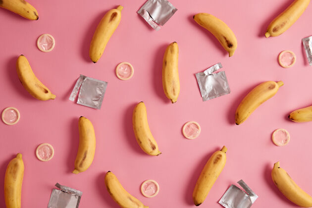 小吃避孕 情色概念黄色香蕉和未包装的避孕套艾滋病意识平躺组成安全的关系粉红色背景保护自己预防性病包装香蕉罗西
