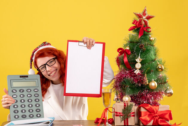 礼物前视图女医生拿着计算器围着圣诞礼物和圣诞树花束丝带圣诞
