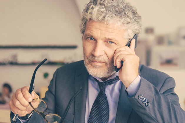 电话正经的成熟商人讲手机 站在同事面前 倚在办公桌上老板男人桌子