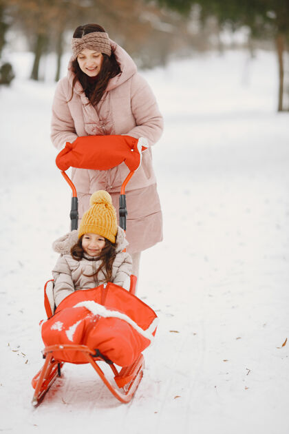 针织品带着雪橇的公园里的女人和小女孩父母自然冬天
