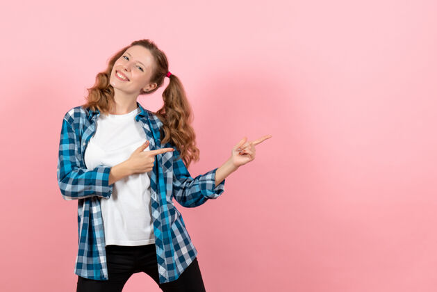 年轻女性正面图：穿着格子衬衫的年轻女性在粉色背景上微笑着摆姿势 女性儿童青春色彩情感模型漂亮孩子服装