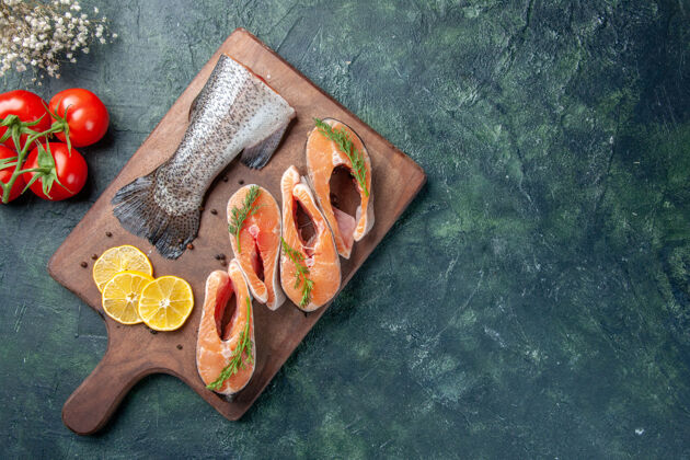 柠檬生鱼片柠檬片绿色胡椒木砧板上的顶视图深色桌子上的西红柿木头锯子生鱼