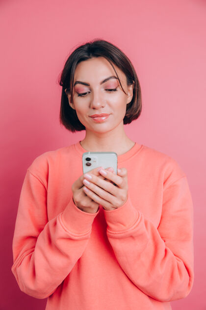 肖像可爱快乐的年轻漂亮的女人用手机在粉红色的墙壁背景上单独摆姿势积极蓝色手机