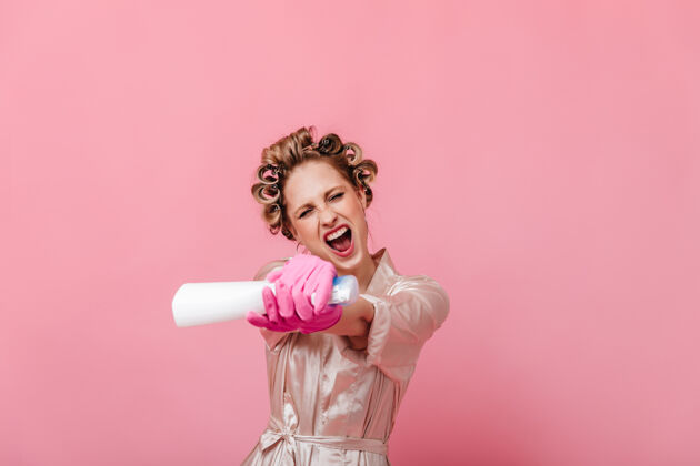 时尚穿着丝袍的活跃主妇喷玻璃清洁剂海绵粉色长袍