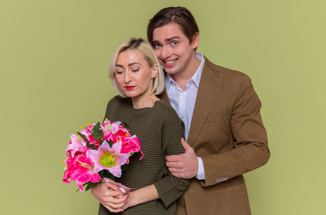 花束年轻美丽的情侣幸福的男人和女人用花束拥抱幸福的爱情一起微笑着庆祝国际妇女节站在绿色的墙上拥抱庆祝快乐