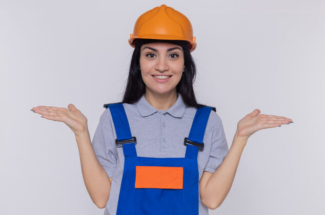 安全身穿施工制服 头戴安全帽的年轻建筑工人站在白色的墙壁上 面带微笑地向两边张开双臂看着前方微笑手臂侧线