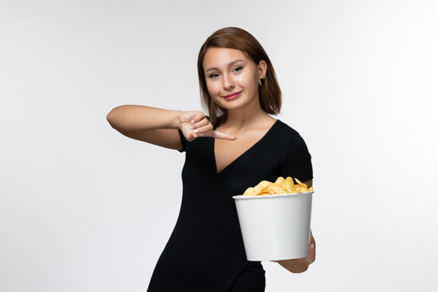 年轻女性正面图身穿黑色衬衫的年轻女性手持薯片 在白色表面摆姿势衬衫土豆剧院