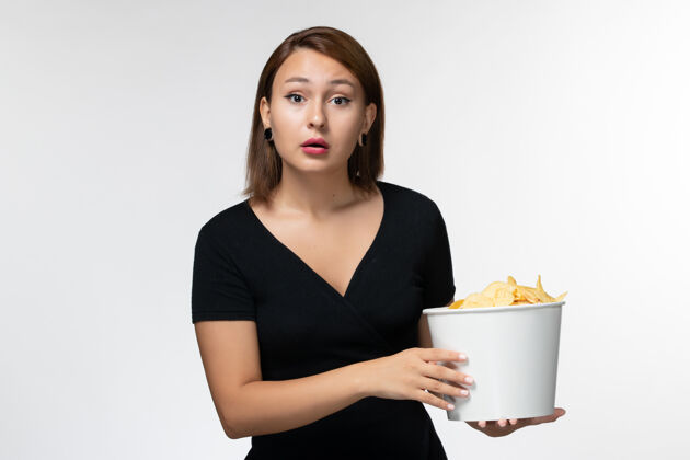 孤独正面图：年轻的女性拿着土豆片的篮子在白色的表面上看电影篮子秘书年轻女性