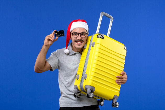 包正面图：年轻男性在蓝色桌面度假飞机上提着包和银行卡前台圣诞节修理工