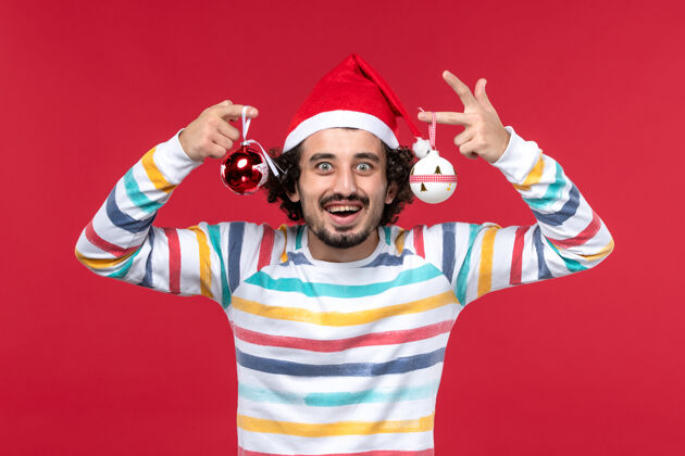 人正面图年轻男子手持圣诞树玩具在红墙新年红色假期娱乐举行年轻男性