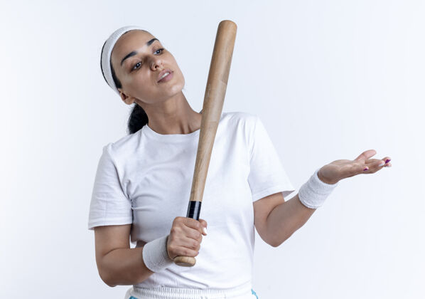 女人年轻自信的白人运动女性戴着头带和腕带拿着球棒看着并指着隔离在空白处的一边蝙蝠腕带空间