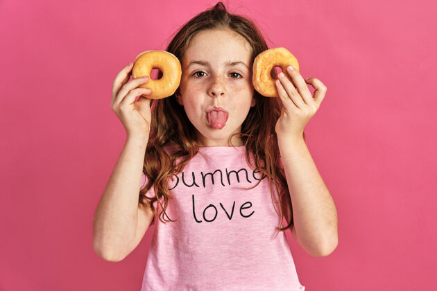 新鲜小女孩在粉红色的墙上摆着几个甜甜圈不健康甜点烘焙