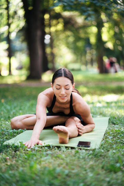 莲花运动型年轻女子早上在公园里做瑜伽 在瑜伽垫上进行女子训练女孩年轻绿色
