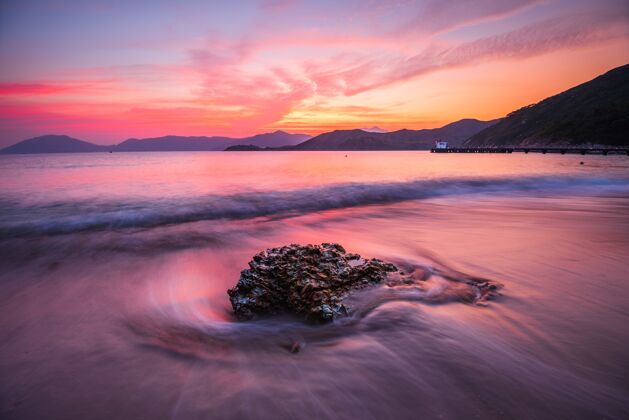 黑暗美丽的高角度拍摄的岩石在波浪的海洋下橙色和粉红色的天空日落光粉色天空