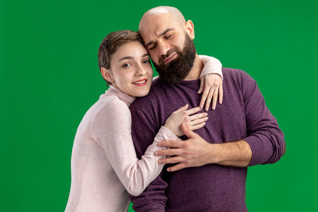 男人一对穿着休闲装的年轻夫妇 一个留着短头发和胡须的女人 在绿色的背景下 一起拥抱庆祝情人节在一起胡须短裤