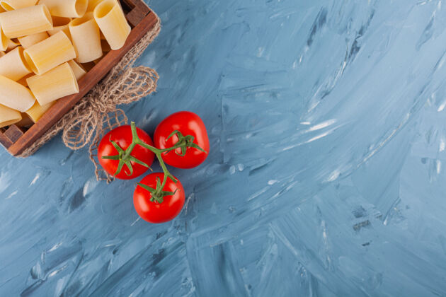 圆形大理石桌上放着一盒干的生面食和新鲜的红色西红柿通心粉碳水化合物背景