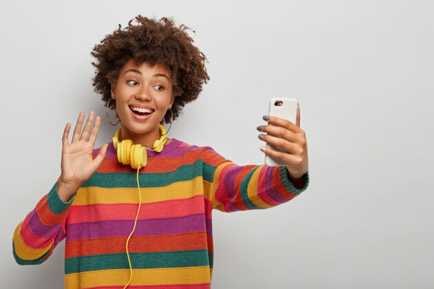 欢呼笑容可掬的非洲裔美国女士通过远程视频通话 对着镜头挥手 向朋友问好 穿着条纹彩色毛衣大笑人精力充沛