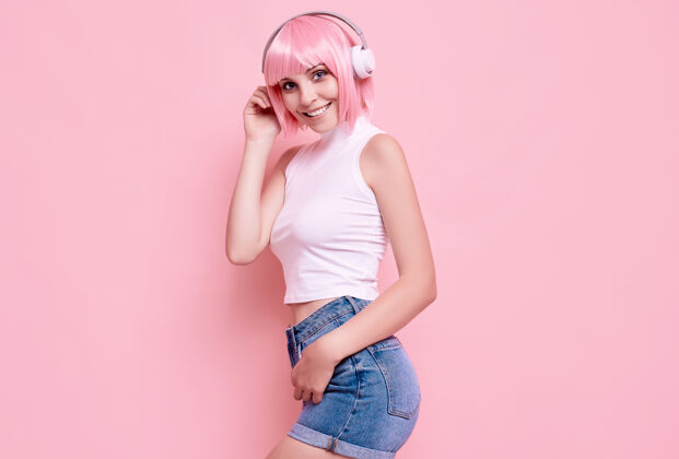 时髦美丽明亮的潮人女孩的肖像与粉红色的头发享受音乐在耳机上五颜六色发型香草音频
