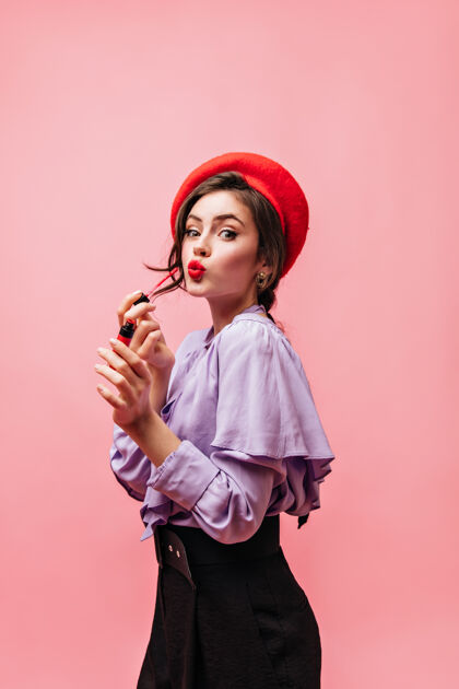 年轻穿着紫色上衣 贝雷帽和裤子的女士的肖像女孩把她的嘴唇画在粉红色的背景上肖像红嘴唇裤子