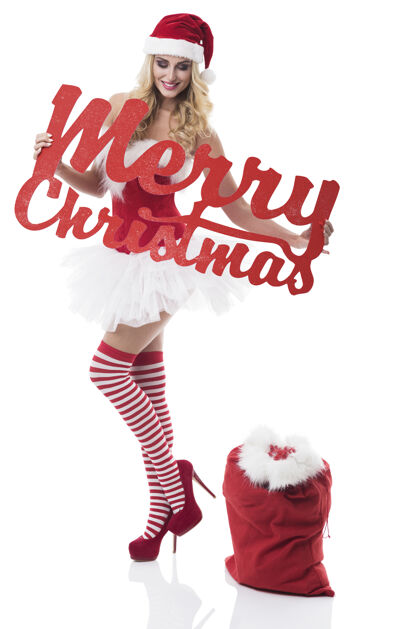 连衣裙穿着圣诞老人服装的性感女人在白墙上摆姿势皮草微笑圣诞快乐
