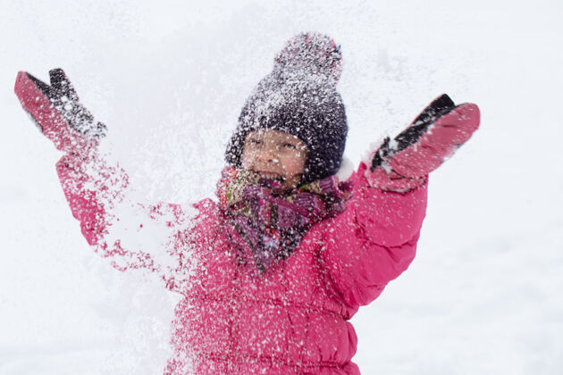 童年一个穿着粉色夹克 戴着帽子的可爱小女孩正在雪地里玩耍冬季儿童娱乐理念游戏娱乐下雪