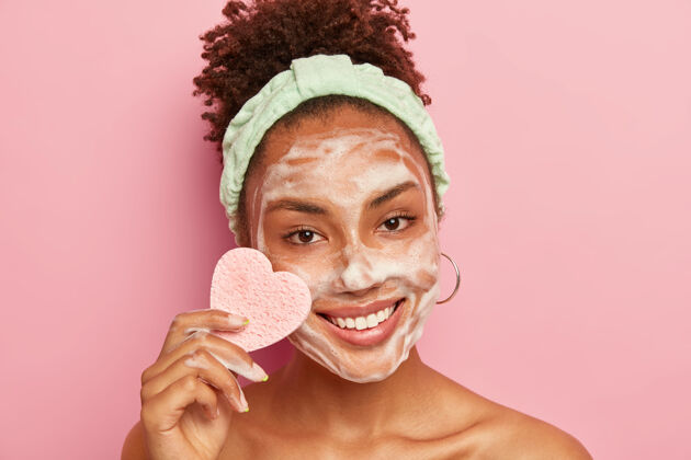 健康快乐女人的肖像拥有完美呵护的肌肤 用泡沫肥皂洗脸 表情愉悦 手持心形海绵擦妆非洲自然清洗