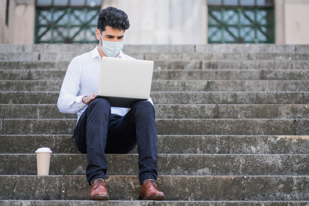 年轻人戴着口罩 坐在室外楼梯上使用笔记本电脑的商人肖像互联网人笔记本电脑
