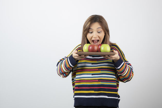 姿势一个穿着便服 吃着一堆苹果的可爱的年轻女人吃肖像盘子