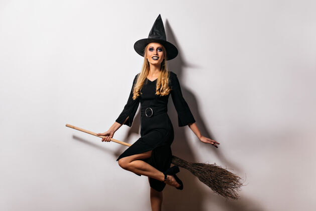 金发可爱的女巫坐在扫帚上戴着魔法帽的可爱的女巫师肖像魔术魔术师