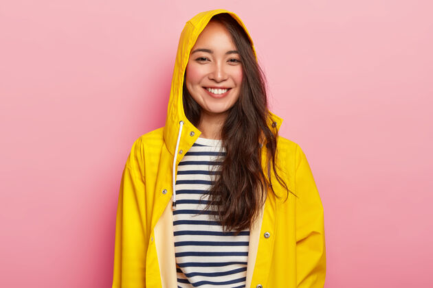 多彩笑容可掬的美女喜欢穿暖和的条纹套头衫 带风帽的黄色雨衣 心情好 雨天和朋友出去玩水手潮湿服装