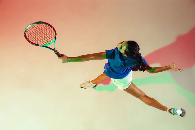训练身穿蓝色球衣的年轻女子正在打网球她用球拍击球室内射门 光线混合年轻 灵活 力量和活力顶视图专业球运动员