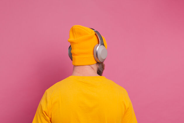 收音机帅哥在随意地听着音乐 用耳机隔离在粉色背景上手势听力男性