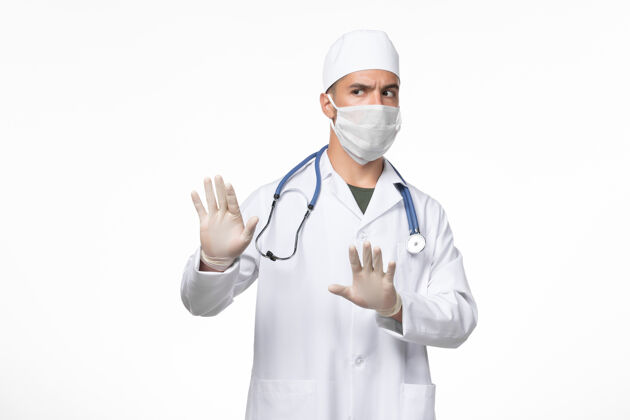 药品正面图：男医生穿着医疗服 戴着口罩 对抗白色墙壁上的冠状病毒病大流行专业人员穿戴正面