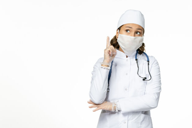 浅白色正面图女医生穿着白色的医疗服 戴着口罩 由于冠状病毒在淡白色的墙壁上大流行病毒疾病隔离冠状病毒无辜口罩专业