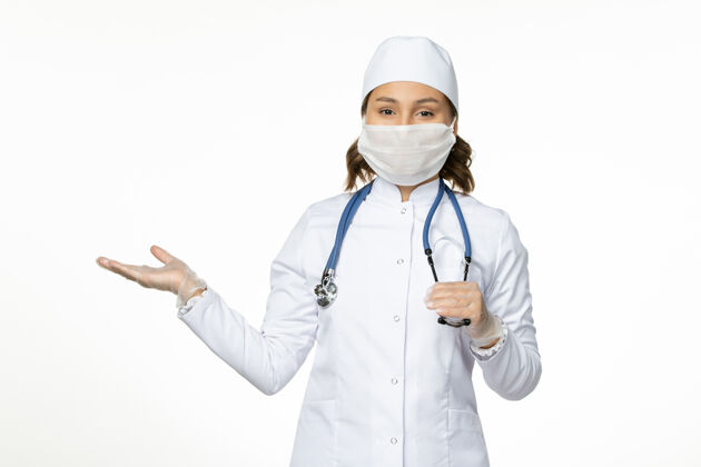 听诊器正面图女医生穿着白色的医疗服 戴着口罩 用听诊器在浅白的办公桌上进行大流行性疾病的药物病毒隔离使用药品医疗