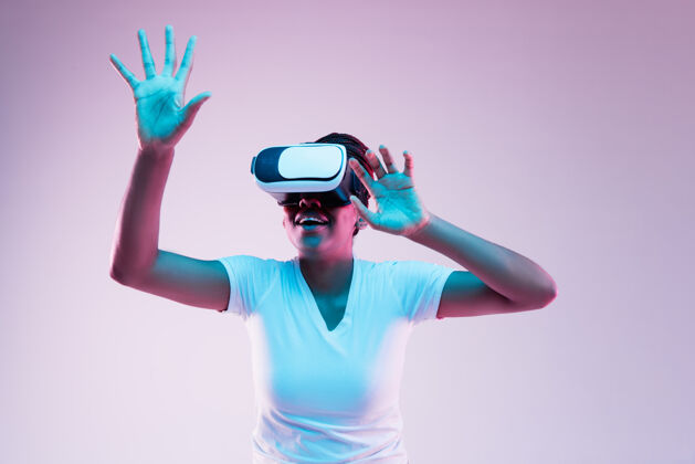 人类年轻的非洲裔美国妇女的肖像玩在虚拟现实眼镜在霓虹灯梯度背景情感面部美国