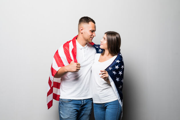 青少年一对漂亮的夫妇手里拿着美国国旗 遮住自己 看着彼此孤立在白色的天空开放享受欢呼