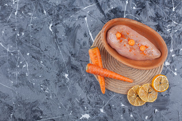 营养鸡胸肉放在碗里 旁边放着胡萝卜和柠檬 放在蓝色的三角架上胡萝卜生的蔬菜