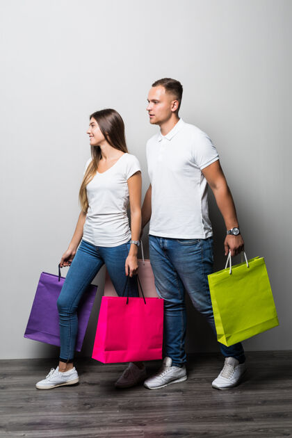 购物者美丽的年轻微笑阳光学生夫妇举行了许多彩色购物袋隔离在白色背景丈夫漂亮休闲