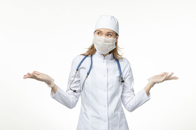 佩戴正面图女医生穿着医疗服戴着口罩戴着手套因白墙上冠状病毒大流行covid-护士冠状病毒预防冠状病毒防护