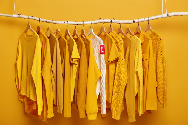 服装衣架上挂满了纯正的黄色女式毛衣一件白色毛衣脱颖而出 正在出售中时尚销售毛衣